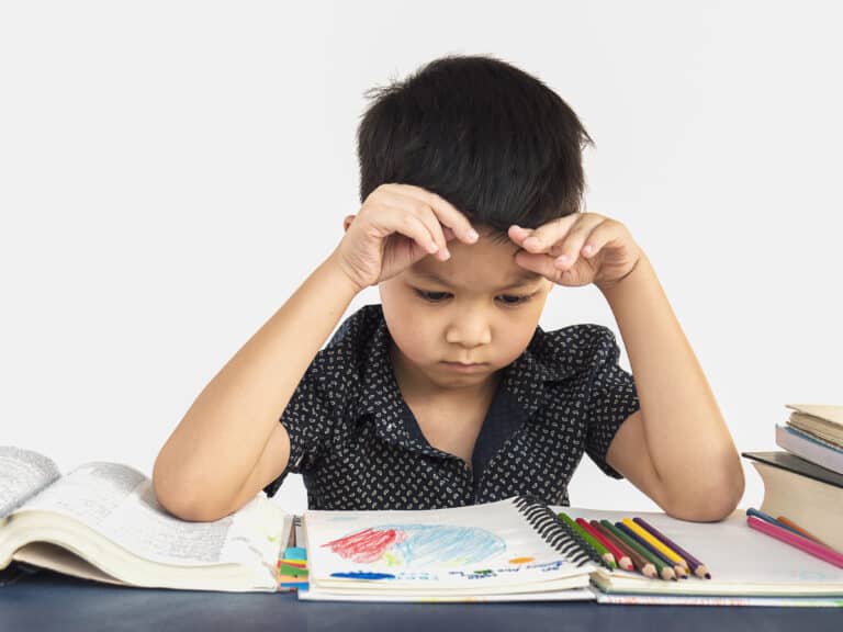 A young boy concentrating intensely on a book, surrounded by colorful pencils.