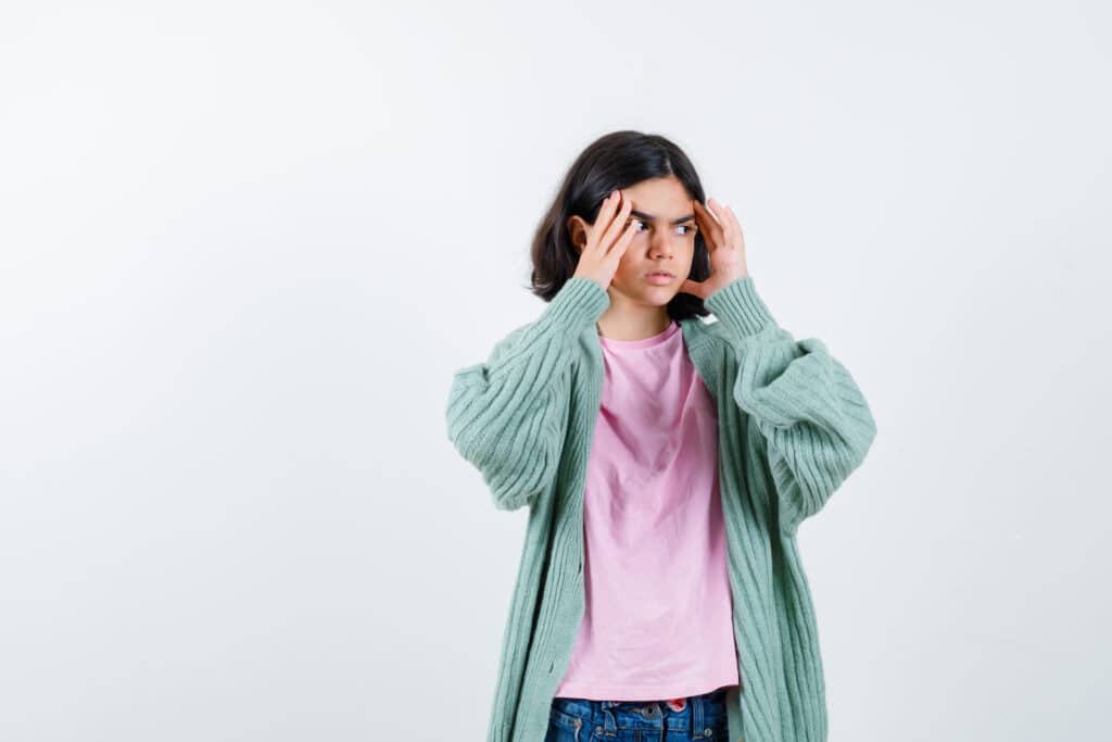 Young woman holding her head with both hands, showing signs of confusion or stress against a white background.
