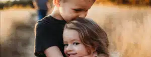 A young boy gently embracing a smiling girl outdoors.